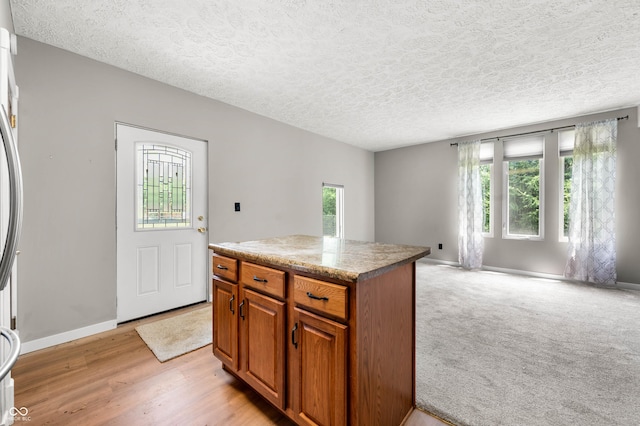 115 Jordan Rd, Indianapolis, IN 46217 - kitchen with brown cabinets, open floor plan, a textured ceiling, a kitchen island, and light wood finished floors