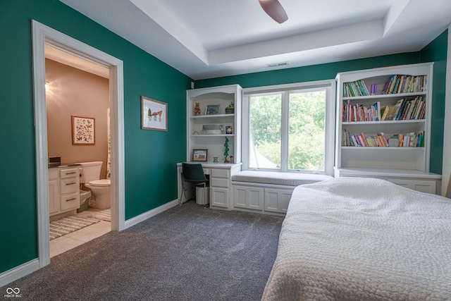 13299 W Wildflower Dr, Columbus, IN 47201 - carpeted bedroom featuring connected bathroom, a tray ceiling, built in desk, and ceiling fan