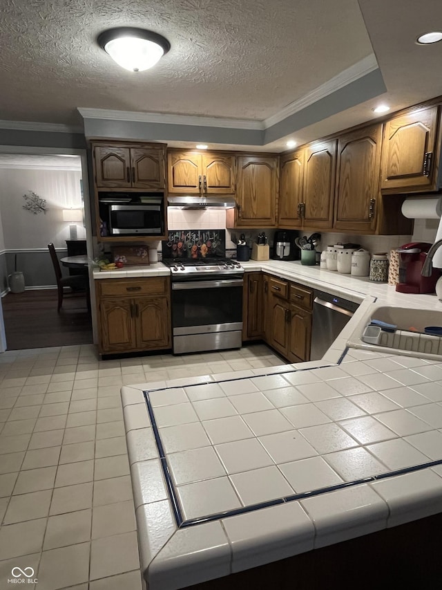 10308 Stormhaven Way, Indianapolis, IN 46256 - kitchen with appliances with stainless steel finishes, ornamental molding, a textured ceiling, under cabinet range hood, and light tile patterned floors