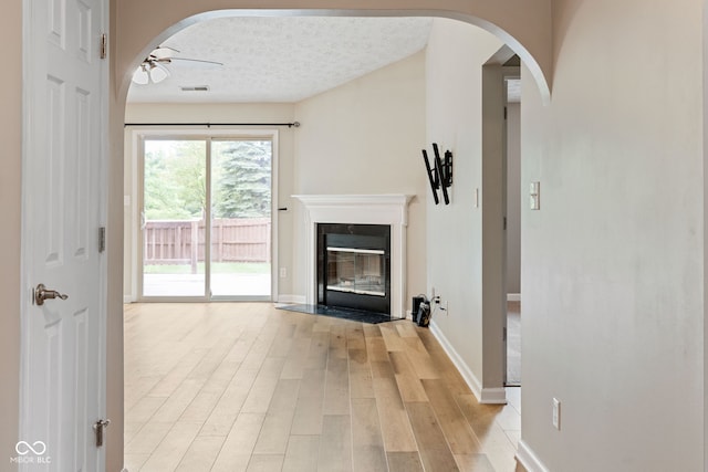 14098 Mimosa Ct, Fishers, IN 46038 - unfurnished living room with ceiling fan, light wood finished floors, a fireplace with flush hearth, arched walkways, and a textured ceiling