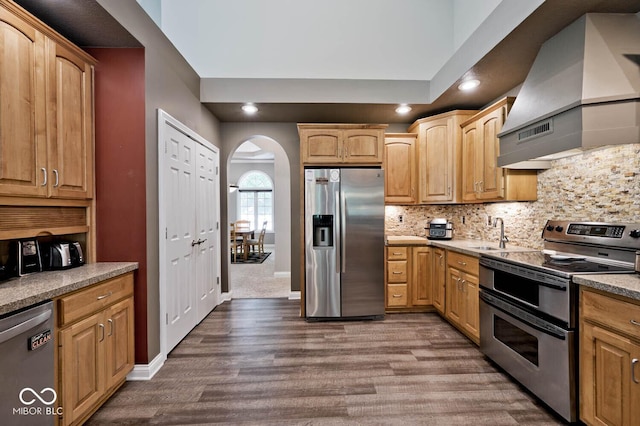 7844 N Timber Run Ct, Indianapolis, IN 46256 - kitchen featuring appliances with stainless steel finishes, wall chimney range hood, arched walkways, dark wood-style flooring, and backsplash