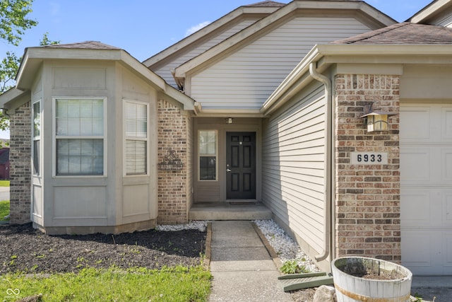 6933 Lohr Way, Indianapolis, IN 46214 - doorway to property featuring an attached garage, brick siding, and roof with shingles