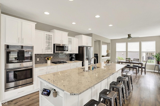 10490 Cleary Trace Dr, Fishers, IN 46040 - kitchen with stainless steel appliances, a kitchen island with sink, white cabinetry, a ceiling fan, and wood finished floors