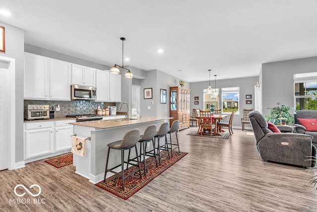 9470 Tobin Cir, Avon, IN 46123 - kitchen featuring stainless steel microwave, wood finished floors, a kitchen island with sink, open floor plan, and healthy amount of natural light