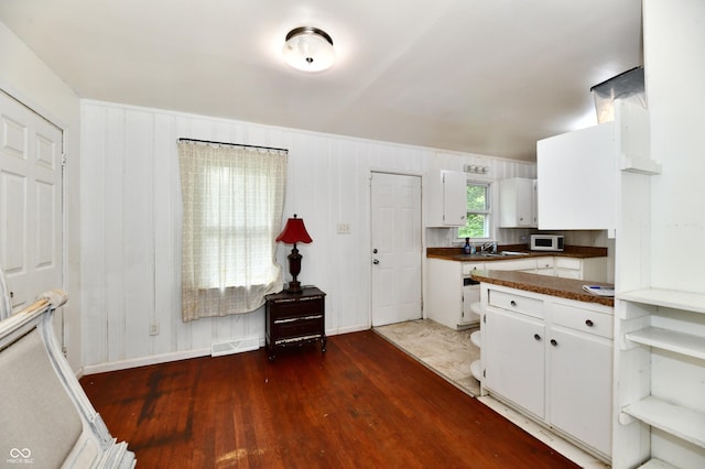 8921 E 21st St, Indianapolis, IN 46219 - kitchen featuring dark countertops, wood finished floors, white cabinetry, and white microwave