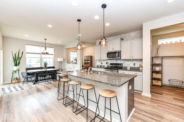 6819 Park Grove Blvd, Whitestown, IN 46075 - kitchen with appliances with stainless steel finishes, a kitchen breakfast bar, a center island with sink, light wood finished floors, and decorative backsplash