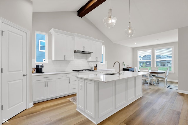 15744 Kohut Ln, Westfield, IN 46074 - kitchen featuring light wood-style floors, decorative backsplash, light countertops, under cabinet range hood, and a center island with sink