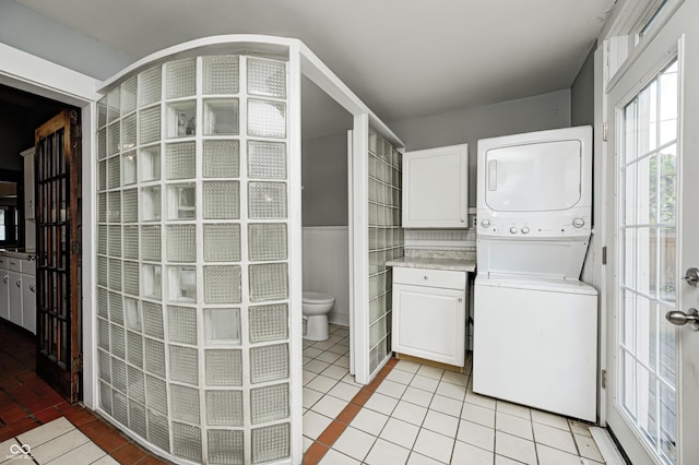 832 Noble St, Indianapolis, IN 46203 - washroom featuring estacked washer and dryer, wainscoting, cabinet space, and light tile patterned floors