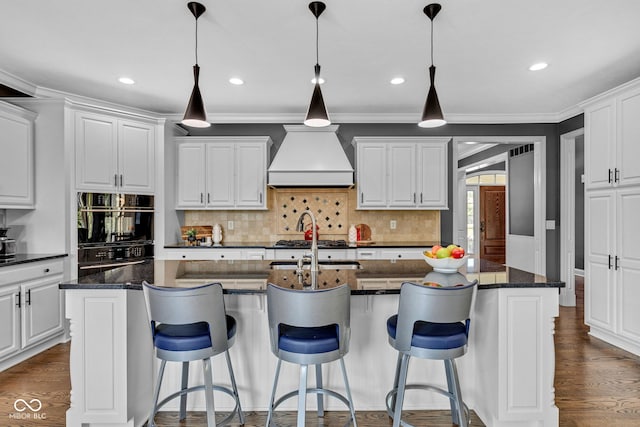 11354 Redwing Ct, Fishers, IN 46037 - kitchen featuring custom exhaust hood, backsplash, an island with sink, white cabinetry, and dark wood-type flooring