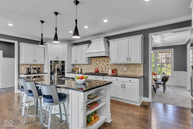 11354 Redwing Ct, Fishers, IN 46037 - kitchen featuring premium range hood, dark countertops, ornamental molding, white cabinetry, and wainscoting