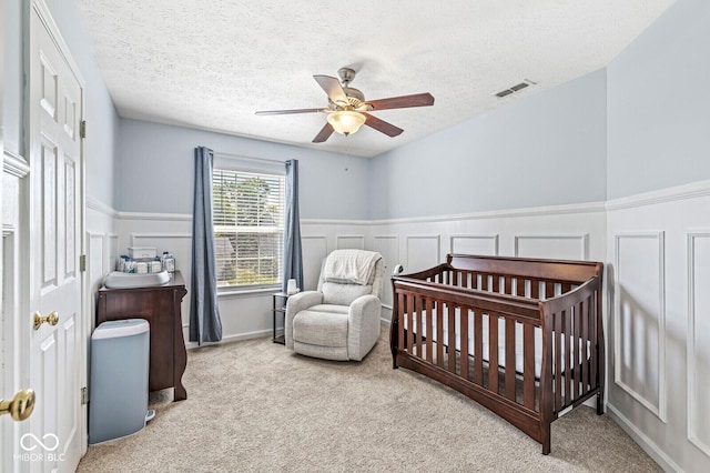 12034 Gatwick View Dr, Fishers, IN 46037 - bedroom with carpet, a nursery area, wainscoting, a textured ceiling, and ceiling fan