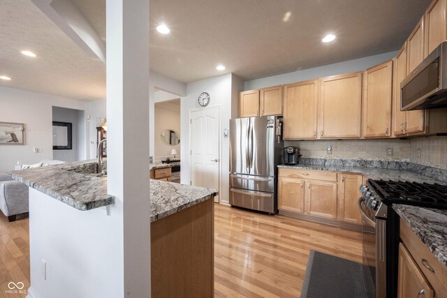 12985 Merlot Ln, Fishers, IN 46037 - kitchen featuring stainless steel appliances, light brown cabinets, light wood-style flooring, decorative backsplash, and light stone countertops