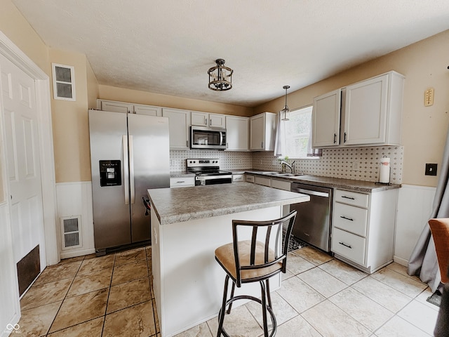 1381 Harrison Dr, Greenwood, IN 46143 - kitchen with appliances with stainless steel finishes, backsplash, a kitchen island, decorative light fixtures, and a wainscoted wall