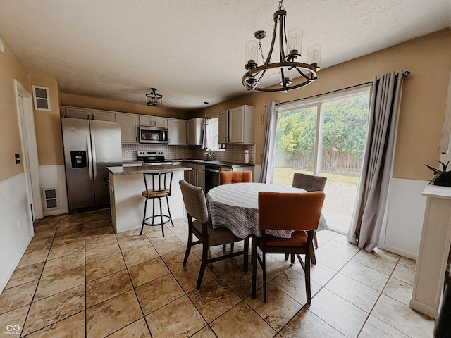 1381 Harrison Dr, Greenwood, IN 46143 - dining area featuring a chandelier, a textured ceiling, a wainscoted wall, and light tile patterned floors
