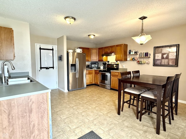 6309 Monteo Dr, Indianapolis, IN 46217 - kitchen featuring stainless steel appliances, under cabinet range hood, brown cabinetry, decorative light fixtures, and a textured ceiling