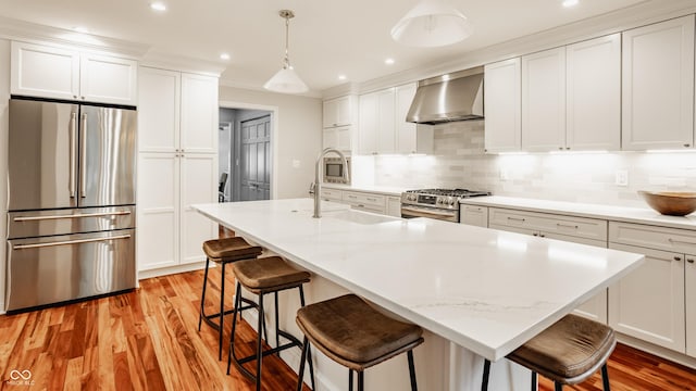 35 E 58th St, Indianapolis, IN 46220 - kitchen featuring stainless steel appliances, wall chimney range hood, light wood-style flooring, white cabinetry, and a breakfast bar area