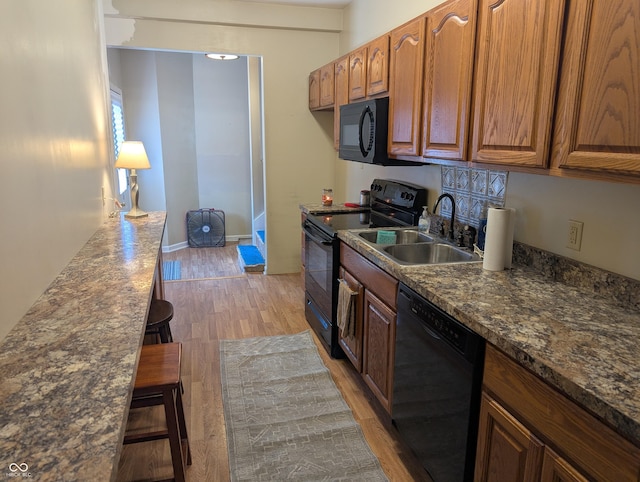 3236 Spruce St, Columbus, IN 47203 - kitchen featuring black appliances, light wood-type flooring, dark countertops, brown cabinets, and a kitchen bar