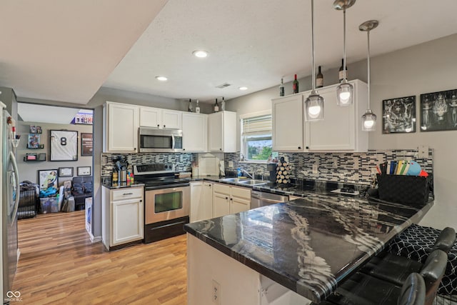 2426 Borgman Ct, Indianapolis, IN 46229 - kitchen featuring appliances with stainless steel finishes, a peninsula, light wood-type flooring, decorative backsplash, and white cabinets