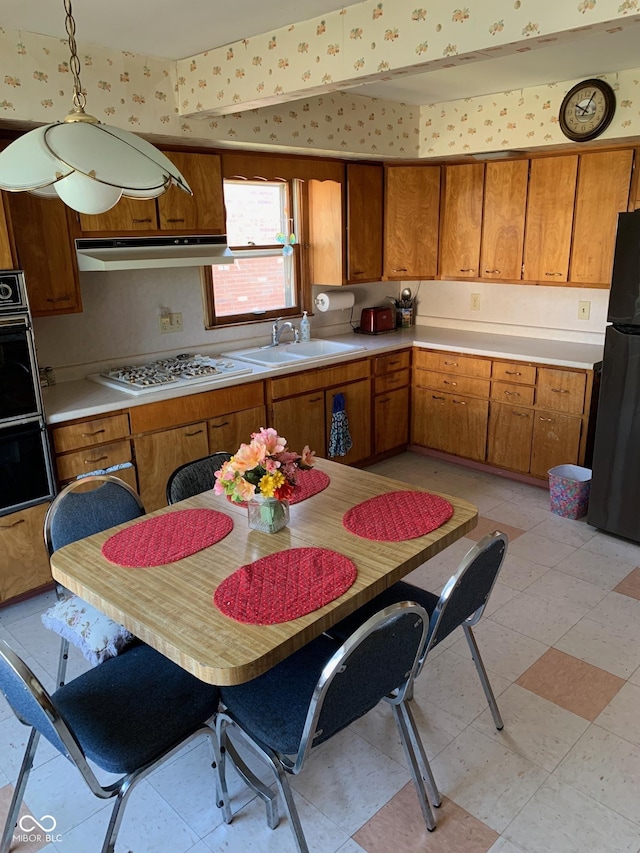 2010 N Winton Ave, Speedway, IN 46224 - kitchen with black appliances, brown cabinets, under cabinet range hood, wallpapered walls, and light countertops
