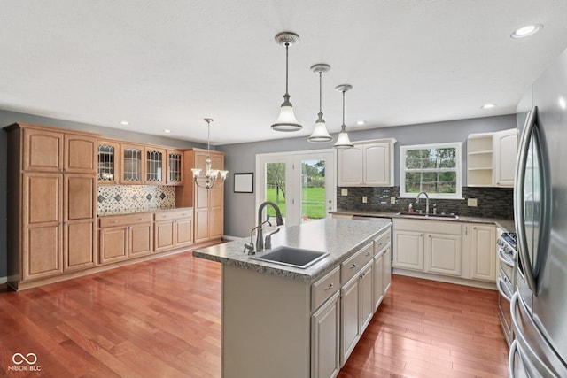151 S St, Southport, IN 46227 - kitchen featuring decorative backsplash, a kitchen island with sink, light wood-style floors, appliances with stainless steel finishes, and hanging light fixtures