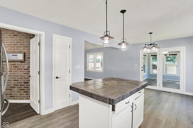 6059 Buck Blvd, Indianapolis, IN 46237 - kitchen with light wood-style floors, brick wall, white cabinetry, tile counters, and decorative light fixtures