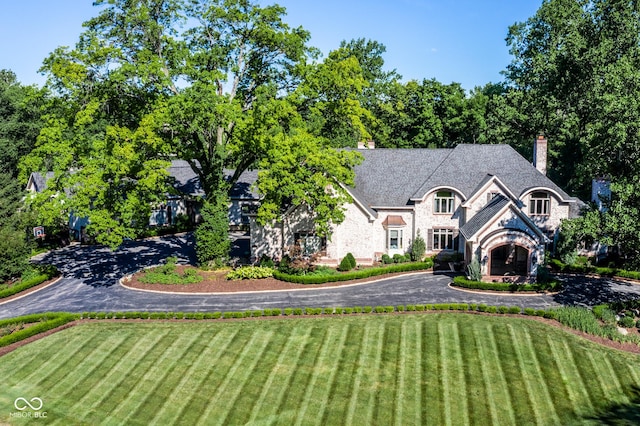 520 Willow Spring Rd, Indianapolis, IN 46240 - french country style house featuring stone siding, a front yard, curved driveway, and a chimney