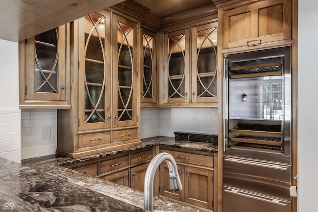 520 Willow Spring Rd, Indianapolis, IN 46240 - kitchen with beverage cooler, decorative backsplash, dark stone counters, glass insert cabinets, and brown cabinetry