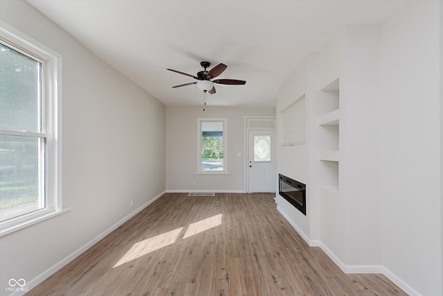 312 E Columbia St, Attica, IN 47918 - unfurnished living room with light wood-type flooring, ceiling fan, a glass covered fireplace, and built in shelves
