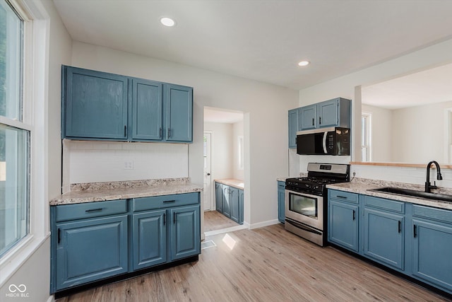 312 E Columbia St, Attica, IN 47918 - kitchen with appliances with stainless steel finishes, blue cabinetry, light wood-style floors, decorative backsplash, and healthy amount of natural light