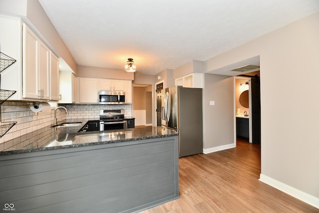 3675 Homestead Cir E, Plainfield, IN 46168 - kitchen featuring stainless steel appliances, backsplash, light wood-style flooring, a peninsula, and dark stone countertops