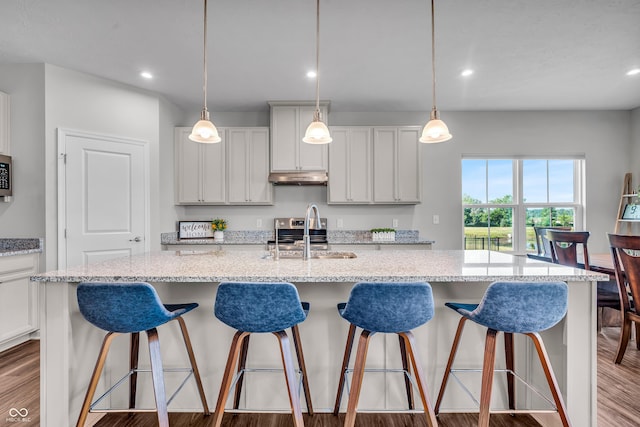 19174 Foley Dr, Westfield, IN 46074 - kitchen featuring under cabinet range hood, wood finished floors, recessed lighting, hanging light fixtures, and light stone counters