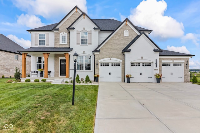 13644 Haven Cove Ln, Fishers, IN 46055 - french provincial home with covered porch, stone siding, concrete driveway, a front lawn, and a shingled roof