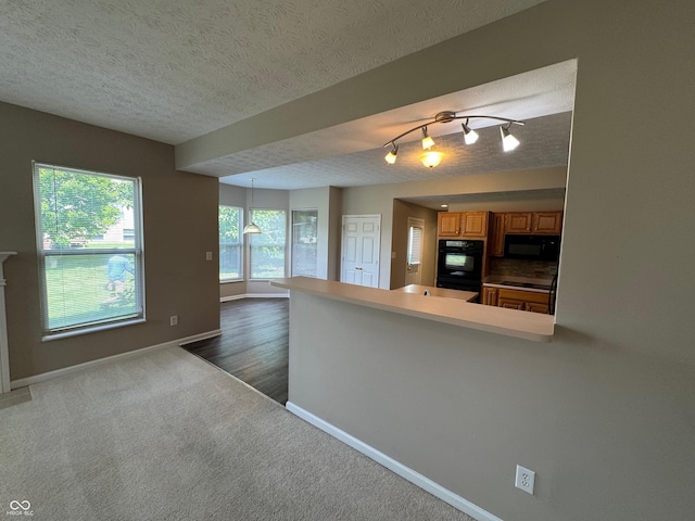 14520 Brackney Ln, Carmel, IN 46032 - kitchen with black appliances, a peninsula, brown cabinets, dark colored carpet, and a textured ceiling