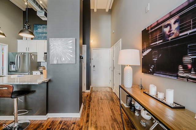 624 E Walnut St Unit 26, Indianapolis, IN 46204 - kitchen featuring a high ceiling, stainless steel fridge with ice dispenser, wood finished floors, white cabinets, and a kitchen bar