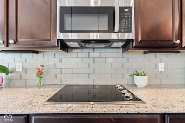 13816 Ambria Dr, Mccordsville, IN 46055 - kitchen with stainless steel microwave, black electric cooktop, dark brown cabinetry, tasteful backsplash, and light stone countertops