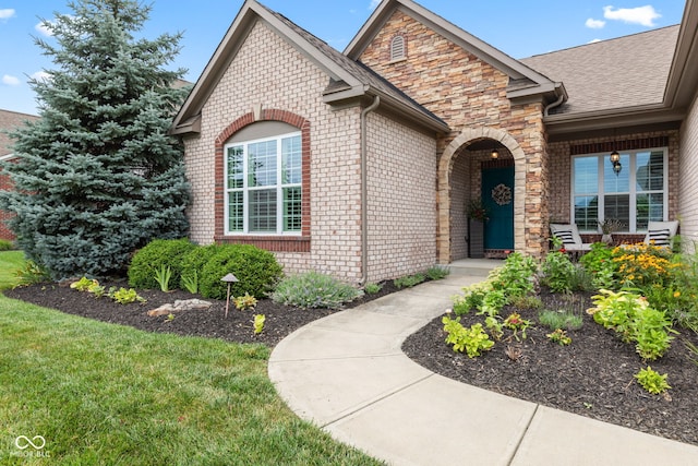 13816 Ambria Dr, Mccordsville, IN 46055 - view of exterior entry with brick siding, a shingled roof, covered porch, a yard, and stone siding