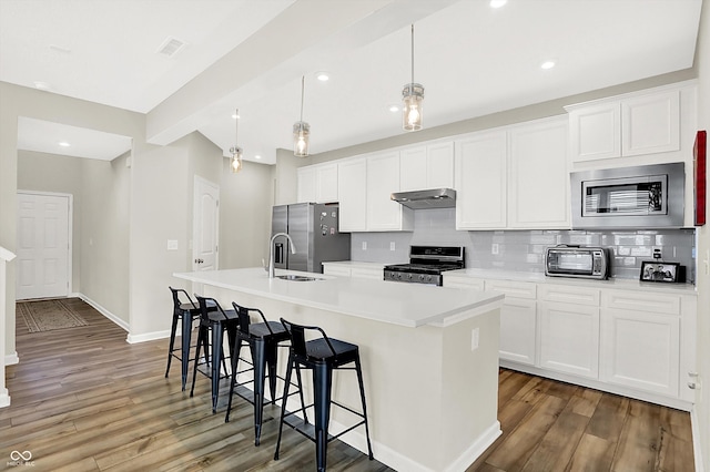 887 Tuxedo Dr, Westfield, IN 46074 - kitchen featuring appliances with stainless steel finishes, under cabinet range hood, an island with sink, wood finished floors, and tasteful backsplash