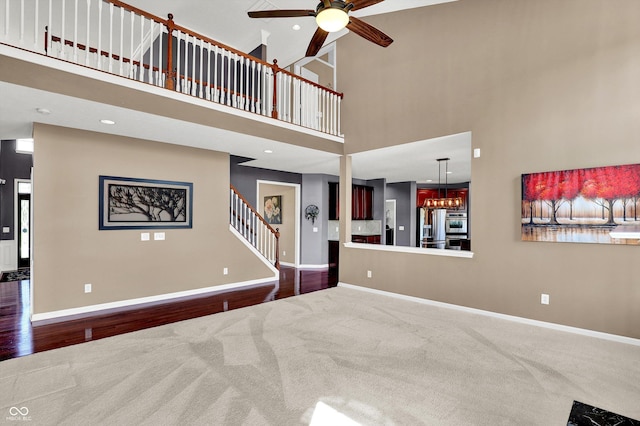 10267 Ranford Blvd, Fishers, IN 46040 - carpeted living room featuring ceiling fan, stairway, a towering ceiling, wood finished floors, and a chandelier