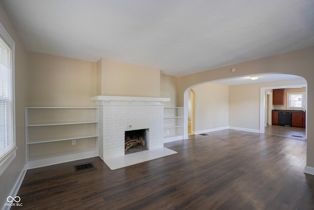 916 E 54th St, Indianapolis, IN 46220 - unfurnished living room with arched walkways, dark wood-style flooring, a fireplace, and built in shelves