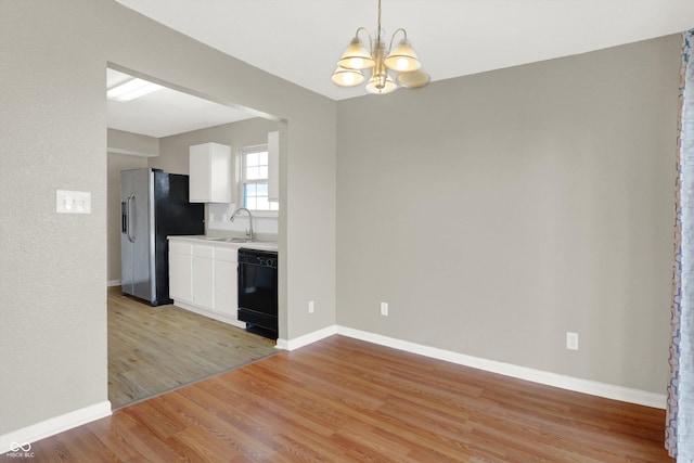 5422 Bluff View Dr, Indianapolis, IN 46217 - kitchen with stainless steel fridge, black dishwasher, a chandelier, light wood finished floors, and white cabinetry