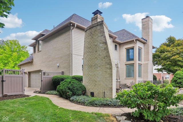12068 Bayhill Dr, Carmel, IN 46033 - view of home's exterior with a chimney, brick siding, roof with shingles, an attached garage, and a gate