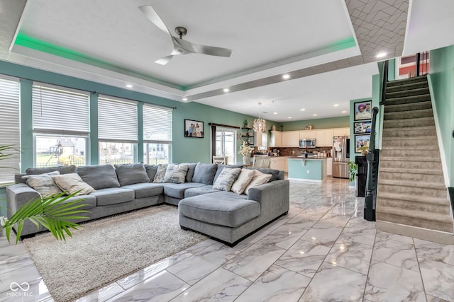 1358 Avocet Dr, Greenwood, IN 46143 - living room featuring a raised ceiling, stairway, a ceiling fan, light marble finish floors, and recessed lighting
