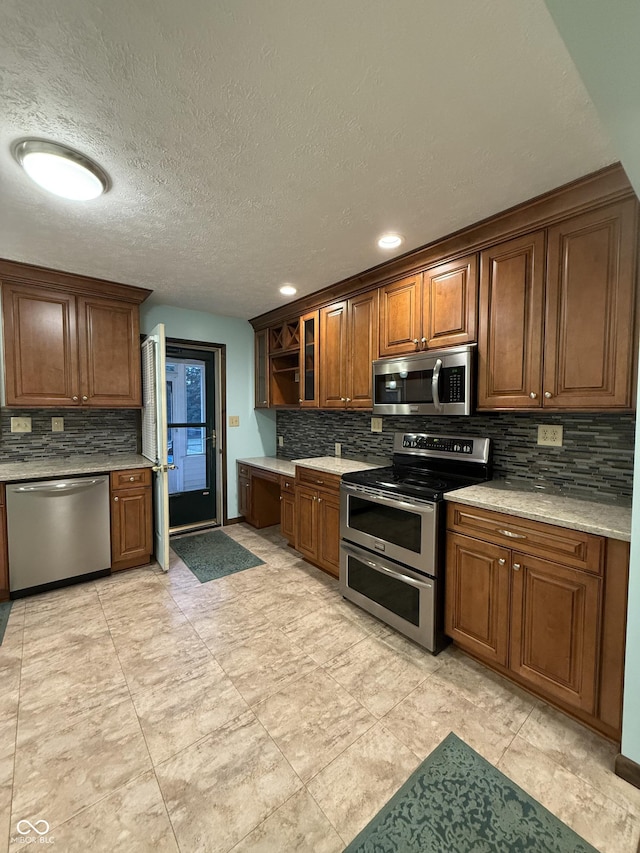 11698 N Bethesda Rd, Mooresville, IN 46158 - kitchen with appliances with stainless steel finishes, tasteful backsplash, light countertops, brown cabinetry, and glass insert cabinets