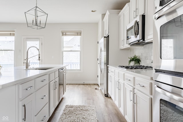 2570 Congress St, Carmel, IN 46032 - kitchen featuring appliances with stainless steel finishes, light wood-style flooring, white cabinets, decorative backsplash, and a chandelier