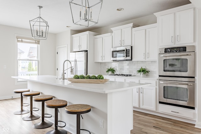 2570 Congress St, Carmel, IN 46032 - kitchen with stainless steel appliances, a center island with sink, light wood-type flooring, backsplash, and white cabinetry