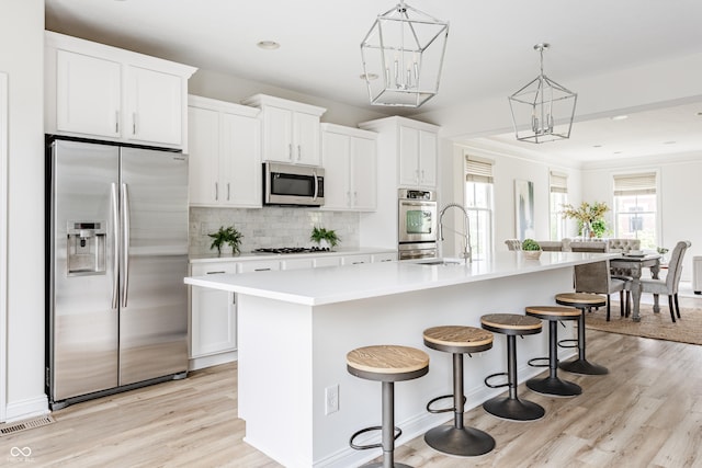2570 Congress St, Carmel, IN 46032 - kitchen with appliances with stainless steel finishes, an island with sink, light wood finished floors, backsplash, and a breakfast bar area