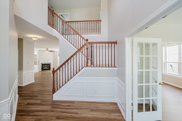 13722 Wendessa Dr, Fishers, IN 46038 - stairway featuring a decorative wall, wood finished floors, a glass covered fireplace, a ceiling fan, and a wainscoted wall