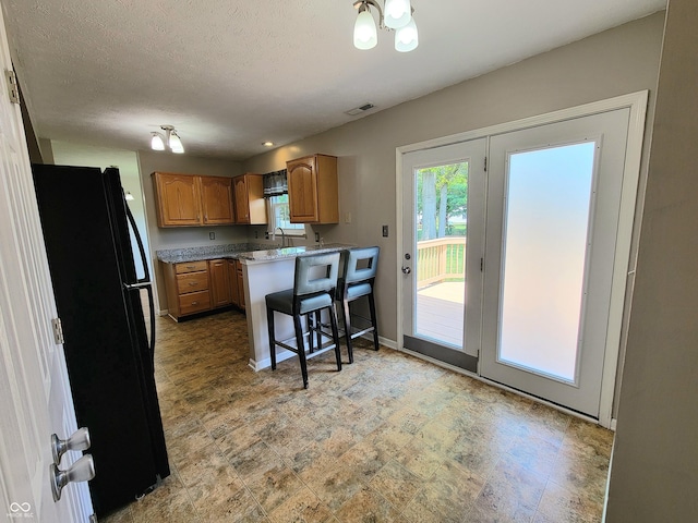 1047 S Jefferson St, Brownsburg, IN 46112 - kitchen with freestanding refrigerator, a kitchen breakfast bar, a peninsula, brown cabinetry, and a textured ceiling