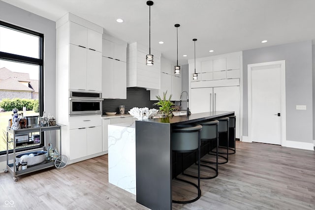 13417 Cambridge Cove Way, Fishers, IN 46055 - kitchen featuring modern cabinets, oven, a kitchen island with sink, light wood finished floors, and recessed lighting