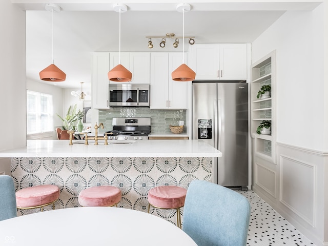 316 Ohmer Ave, Indianapolis, IN 46219 - kitchen featuring appliances with stainless steel finishes, decorative backsplash, light countertops, white cabinets, and pendant lighting
